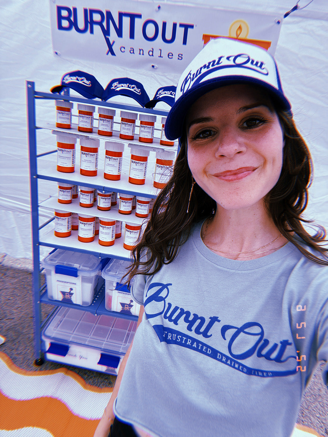 Person wearing a 'Burnt Out' branded cap and t-shirt standing next to a display of candles.