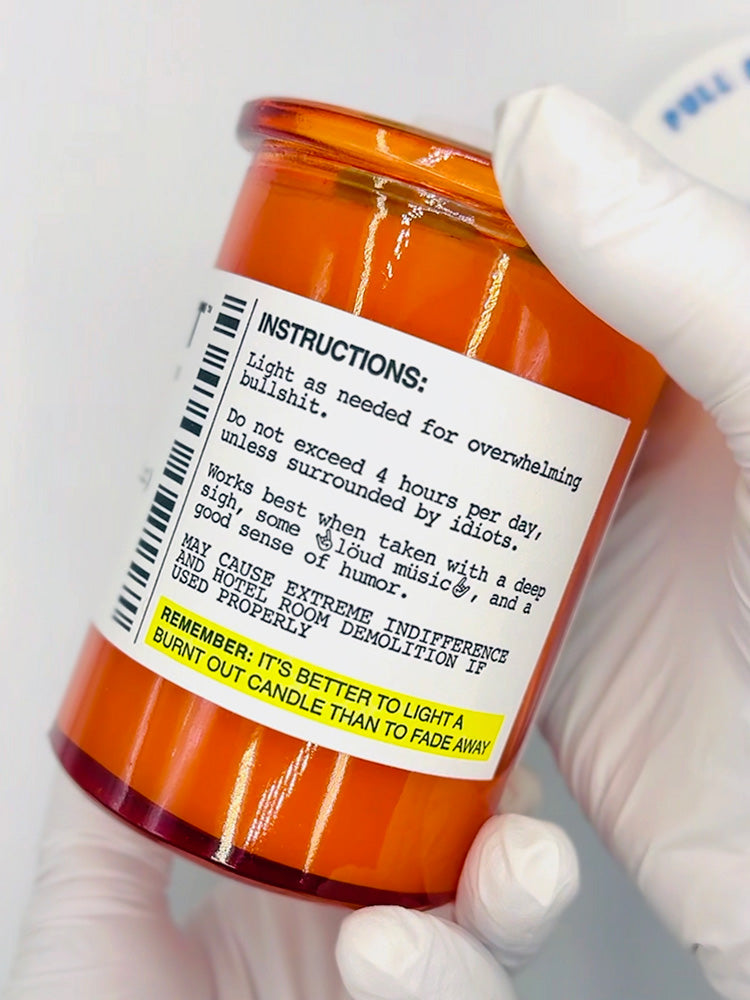 Orange jar with humorous label instructions held by a gloved hand against a white background