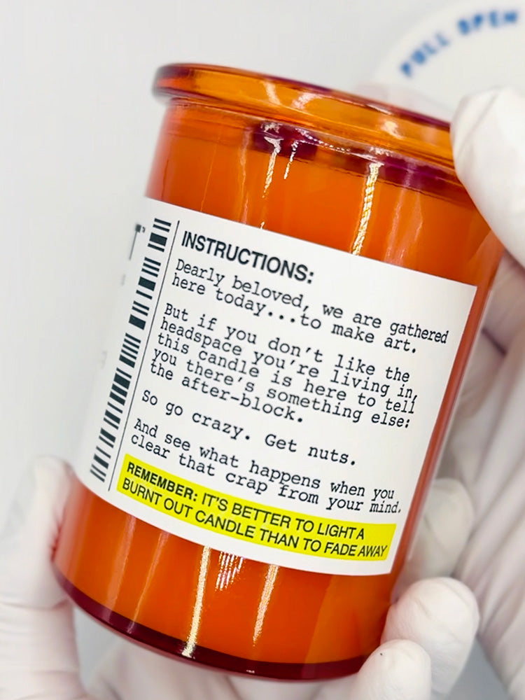 Orange candle jar with a label held by a gloved hand on a white background