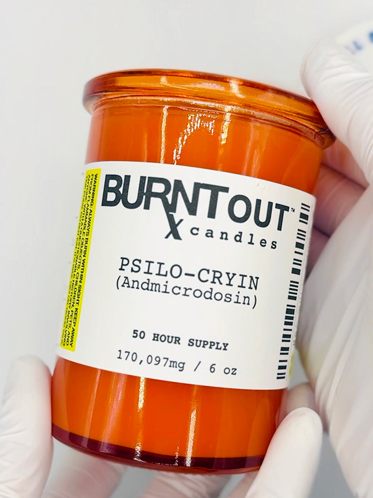 Orange candle labeled  'Burnt Out Candles' held by gloved hands on a white background