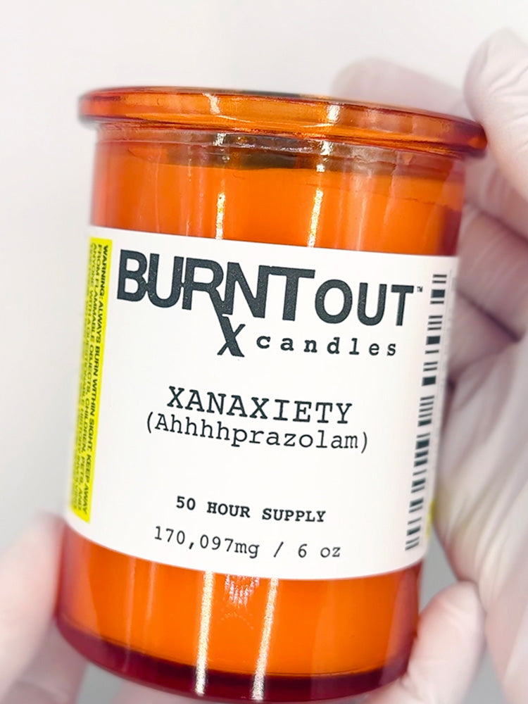 Pharma-satire candle labeled 'Burnt Out Candles' held by a gloved hand.